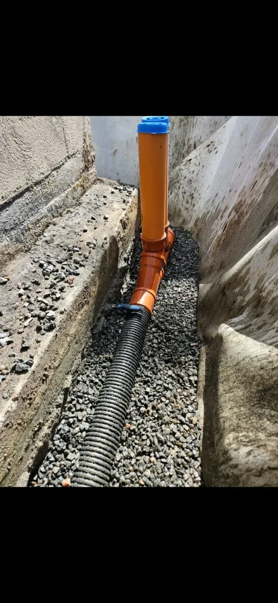 Svarta dräneringsrör i makadam längs husgrund